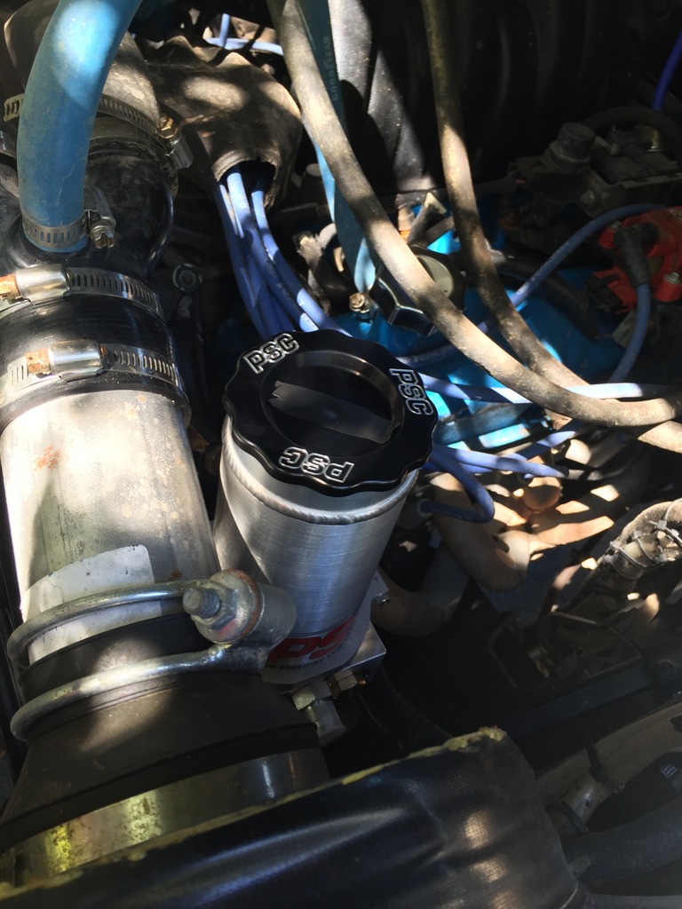 Engine bay with a silver PSC reservoir and black cap, surrounded by hoses and wires