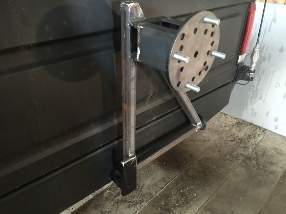 Custom spare tire carrier mounted on the rear of a dark vehicle.