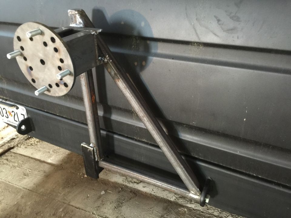 Custom steel spare tire carrier mounted on the rear of a dark vehicle.