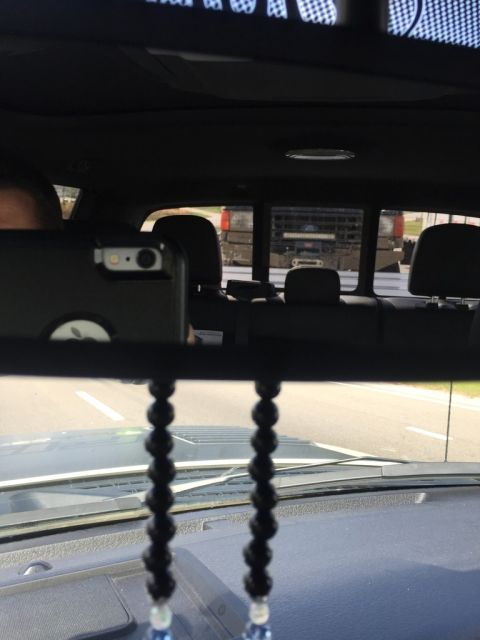 1989 Ford Bronco - Reflection in the rearview mirror shows the rear of a dark-colored pickup truck with a light bar mounted above the windshield. The interior…
