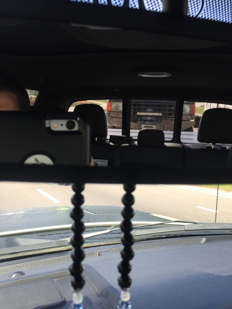 Reflection of a pickup truck in the rearview mirror, with interior details in the foreground.