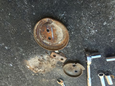 1989 Ford Bronco - Two rusty metal circular objects with holes are on a dark, textured surface, possibly concrete. Several metal tools, including a ratchet an…
