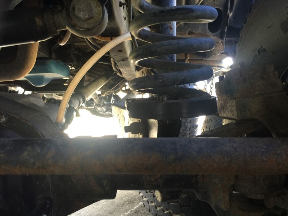 Undercarriage of a vehicle showing suspension, coil spring, tire, and a yellow hose.