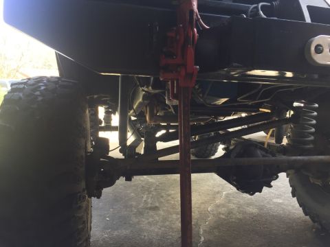 1989 Ford Bronco - The underside of a vehicle, likely an SUV or truck, is shown with a red Hi-Lift jack positioned to lift the frame. Visible components inclu…