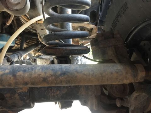 1989 Ford Bronco - This is a close-up, low-angle shot of the suspension system of a 1989 Ford Bronco. The image focuses on the rusty coil spring, shock absorb…