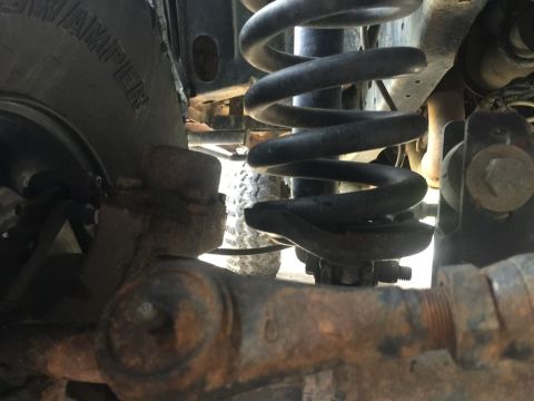 1989 Ford Bronco - A close-up view of the suspension system of a vehicle, showing a coil spring, a tire with the word "SWAMPER" visible, and rusty metal compo…
