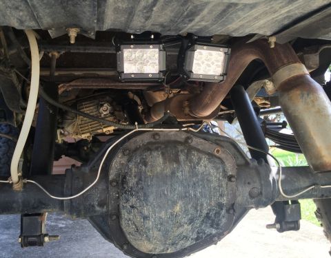 1989 Ford Bronco - The underside of a vehicle shows a large rear differential, exhaust system, and two aftermarket LED light pods mounted to the frame.