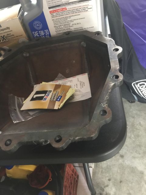 1989 Ford Bronco - A close-up view shows a metal oil pan with several bolt holes and some receipts and a Mobil 1 oil sample packet inside. A bottle of Mobil 1…