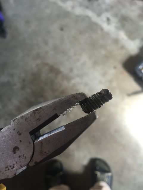 1989 Ford Bronco - A close-up shot shows a pair of pliers holding a damaged, threaded metal bolt with debris on it. The background is a blurry concrete surfac…