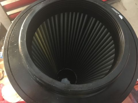 1989 Ford Bronco - Close-up overhead view of a black conical air filter with pleated media, housed within a black threaded adapter. The filter is positioned i…