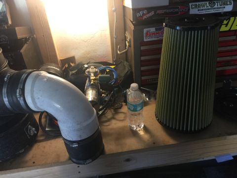 1989 Ford Bronco - A large, conical air filter with a yellow element sits on a workbench next to a plastic water bottle and a section of large diameter white…