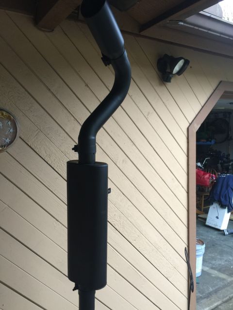 1989 Ford Bronco - A black exhaust pipe and muffler assembly is mounted vertically on the side of a building with tan horizontal siding. The exhaust pipe curv…