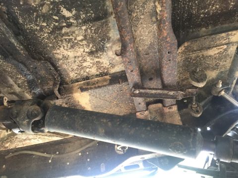 1989 Ford Bronco - Underside view of a 1989 Ford Bronco showing the driveshaft, universal joint, and rusted frame components. The vehicle appears to be dirty…