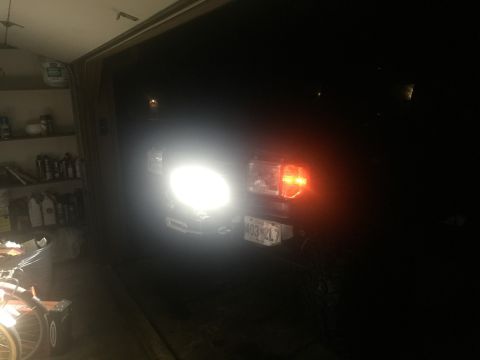 1989 Ford Bronco - The front of a dark-colored vehicle, likely a Ford Bronco, is illuminated by its bright headlights and amber turn signal. The vehicle is pa…
