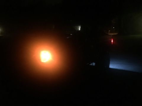 1989 Ford Bronco - A close-up of a vehicle's glowing orange turn signal at night. The vehicle is dark and appears to be parked on a paved surface.