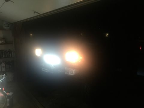 1989 Ford Bronco - The front of a dark-colored vehicle, possibly a 1989 Ford Bronco, is visible in a dimly lit garage. The headlights are illuminated, with th…