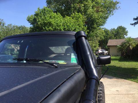 1989 Ford Bronco - A black SUV with a snorkel intake is parked on a paved driveway in front of a house. The vehicle's hood and windshield are visible, along w…