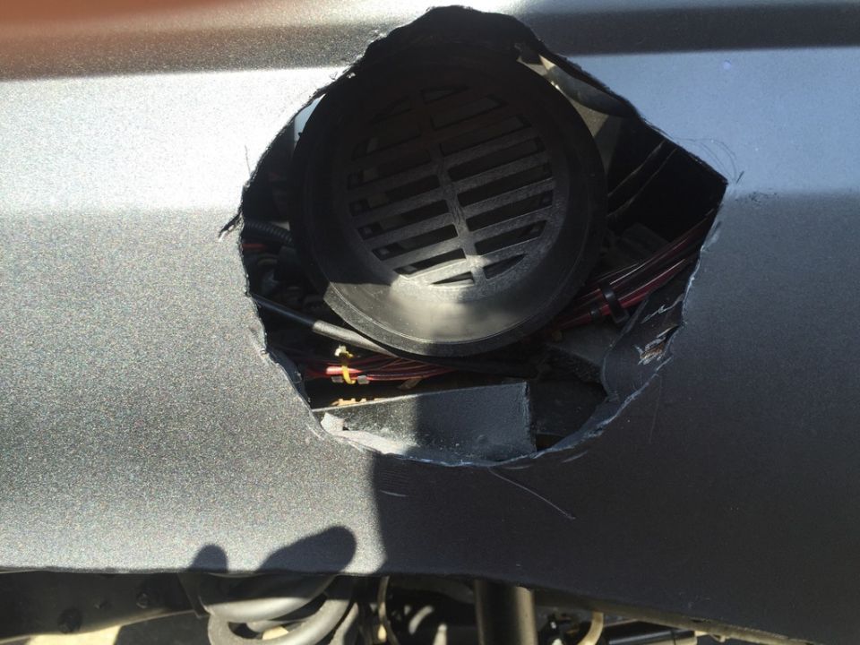 Cutout in gray vehicle body revealing black grille and exposed wiring