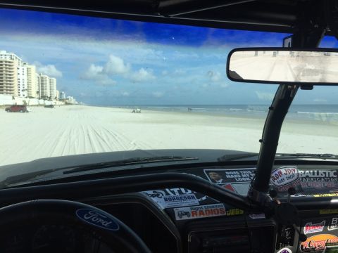 1989 Ford Bronco - Driving a Ford Bronco on the beach, with the ocean and buildings visible through the windshield.