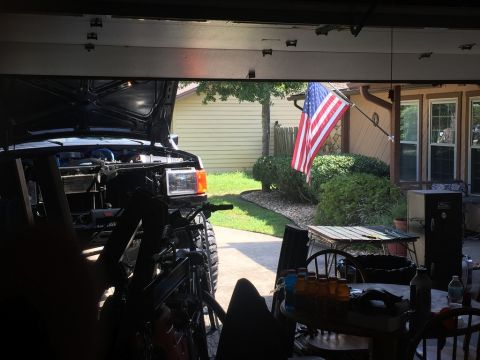 1989 Ford Bronco - View of a black SUV with its hood open, parked in a driveway with an American flag flying.