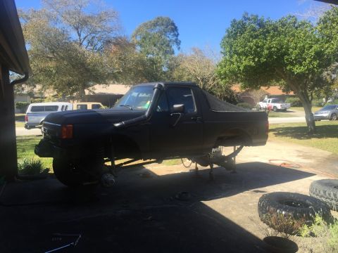 1989 Ford Bronco - A black 1989 Ford Bronco is shown with its front end lifted on jack stands, undergoing maintenance. The vehicle has a snorkel intake on the…