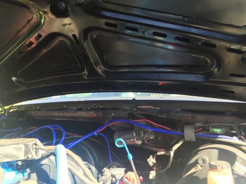 1989 Ford Bronco - The underside of a black hood is open, revealing a complex engine bay with blue and red wiring looms. Various engine components and hoses a…