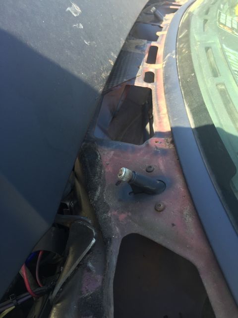 1989 Ford Bronco - A close-up view of the cowl area of a vehicle, showing rusted metal, wiring, and a black plastic component with a silver-capped adjustment…