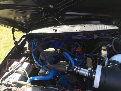 1989 Ford Bronco - The engine bay of a modified vehicle, featuring a black hood, blue hoses, and a large black air intake. The vehicle appears to be a truck o…