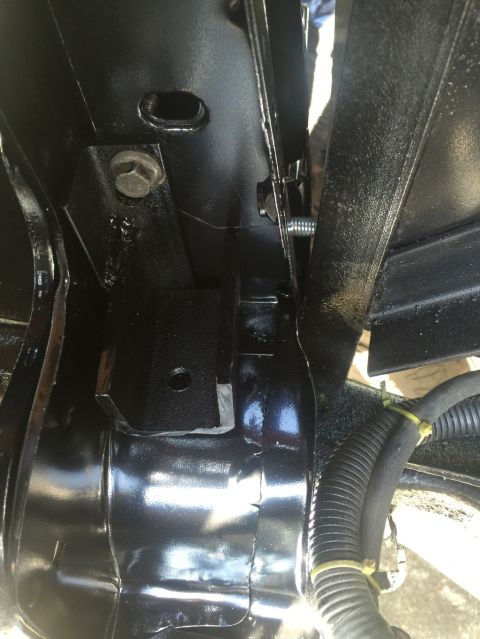 1989 Ford Bronco - A close-up view shows a black painted metal bracket bolted to a vehicle frame. A black corrugated wire loom is secured with yellow zip ties…