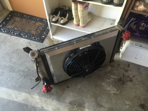 1989 Ford Bronco - A radiator with an electric fan attached is lying on a concrete floor next to a white Igloo cooler and a shelf with shoes and boots.