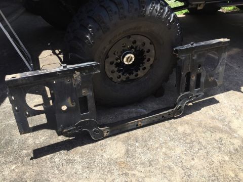 1989 Ford Bronco - A black metal radiator support assembly is laid out on a concrete surface in front of a large off-road tire. The assembly has cutouts for h…