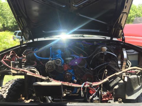 1989 Ford Bronco - The open hood of a black Ford Bronco reveals a detailed view of its engine bay, featuring a blue-painted engine block and numerous blue hos…