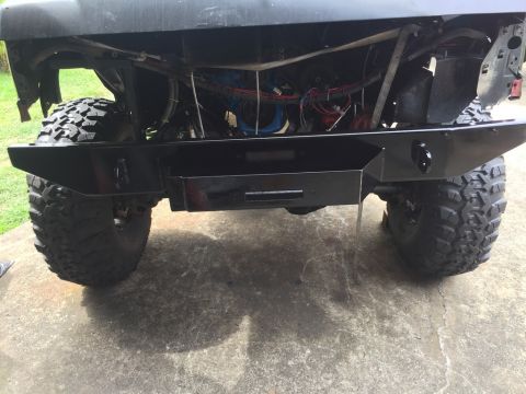 1989 Ford Bronco - The front of a black Ford Bronco is shown with a custom black steel bumper installed. The vehicle has large, aggressive off-road tires.