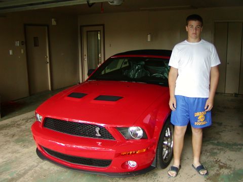 2007 Ford Mustang - A red 2007 Ford Mustang is shown parked in a garage with a person standing beside it.