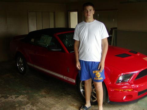 2007 Ford Mustang - A young man poses with a red 2007 Ford Mustang convertible, showing off the car's side profile and front end.