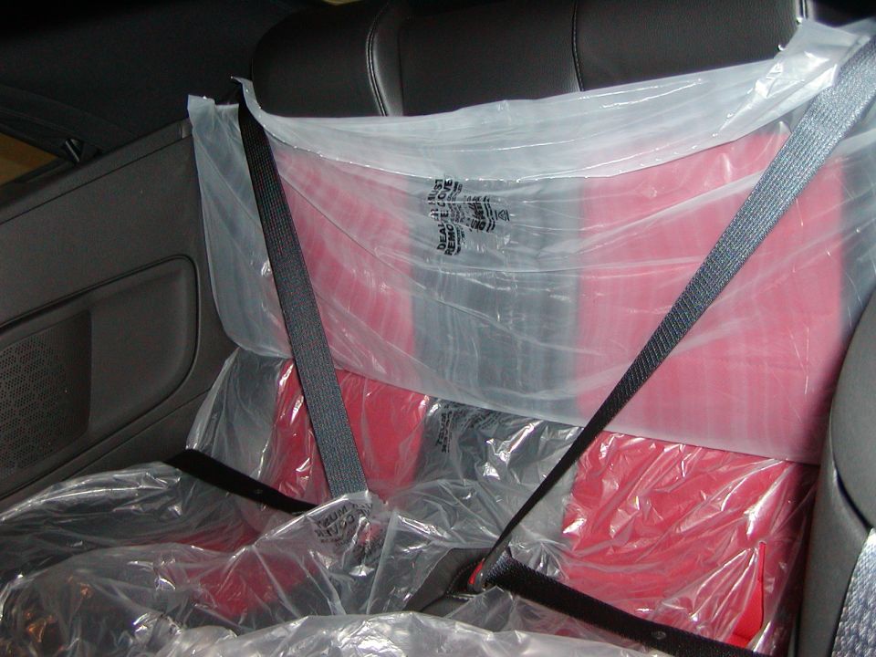 Interior view of red car seats covered in plastic and secured by seat belts.