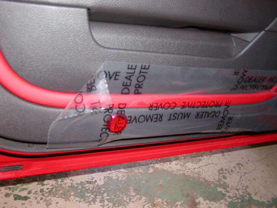 Red interior trim on a car door panel covered by protective plastic with text