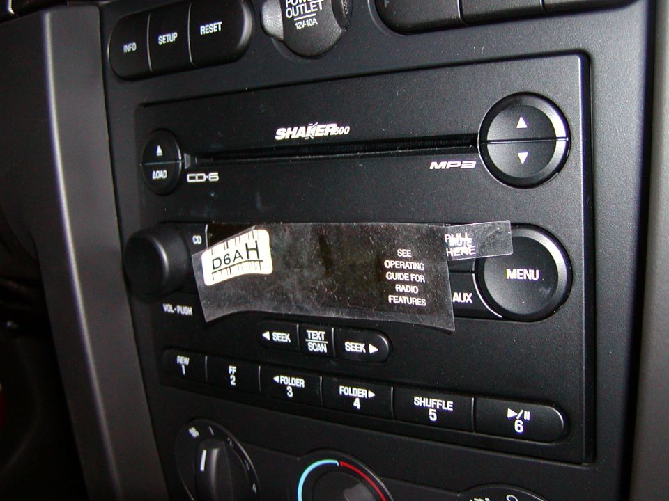 Close-up of a car stereo system with buttons and a CD slot, featuring a sticker with text.