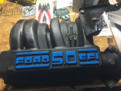 1989 Ford Bronco - A black Ford 5.0 EFI intake manifold with blue lettering is displayed on a wooden surface, surrounded by tools and parts.