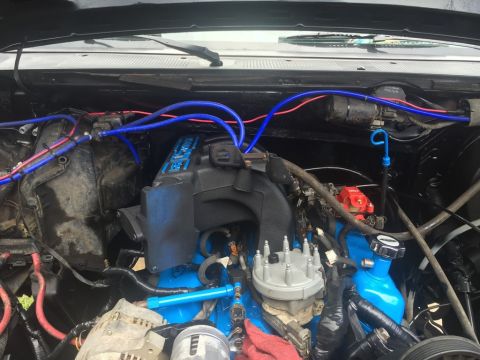 1989 Ford Bronco - Close-up view of a modified engine bay, likely from a Ford Bronco, featuring bright blue painted engine components, blue and red hoses, and…