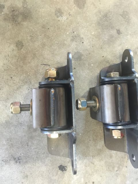 1989 Ford Bronco - Two custom metal brackets with rubber bushings and hardware are shown mounted on a concrete surface. The brackets appear to be part of a su…