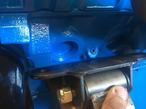 1989 Ford Bronco - A close-up view shows a blue painted engine block with a metal bracket and rubber bushing assembly attached with a bolt and nut.