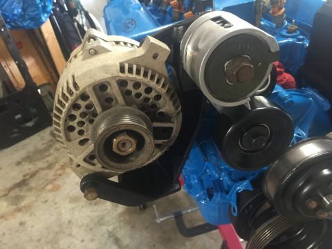 1989 Ford Bronco - A close-up view of an alternator and belt tensioner assembly mounted on a blue engine block. The alternator is dusty and shows signs of wea…