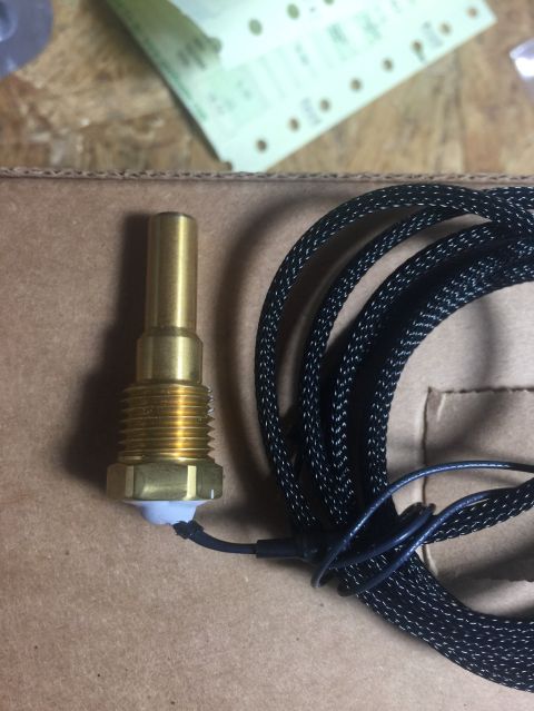 1989 Ford Bronco - A brass temperature sensor with a black braided cable is shown resting on a cardboard surface. The sensor has threaded fittings and a white…