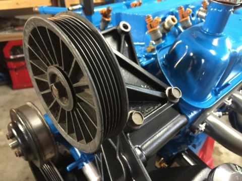 1989 Ford Bronco - A close-up view of a V-belt pulley system attached to a blue engine block with fuel injectors visible. The pulley system includes a large r…