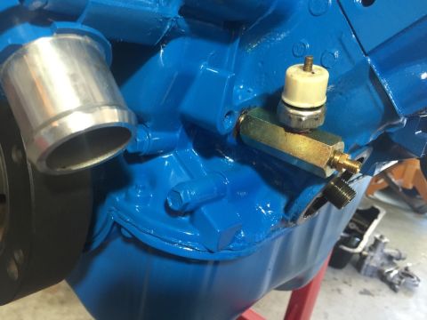 1989 Ford Bronco - Close-up of a blue engine block a brass coolant sensor and a silver hose adapter, with 'SUPERMOTORS' visible at the bottom.