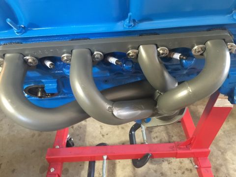 1989 Ford Bronco - A close-up view shows a set of gray exhaust headers bolted to the side of a blue engine block. Several spark plugs are visible between the…