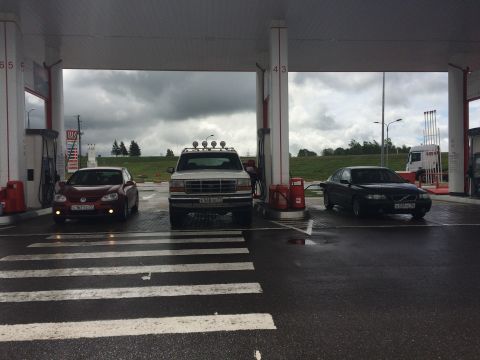 1993 Ford Bronco - A white Ford Bronco with roof lights is parked at a gas station, alongside other vehicles.