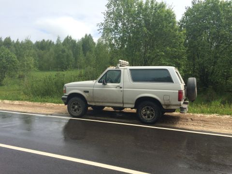 1993 Ford Bronco - A white Ford Bronco is parked on the side of a road after a rain shower.