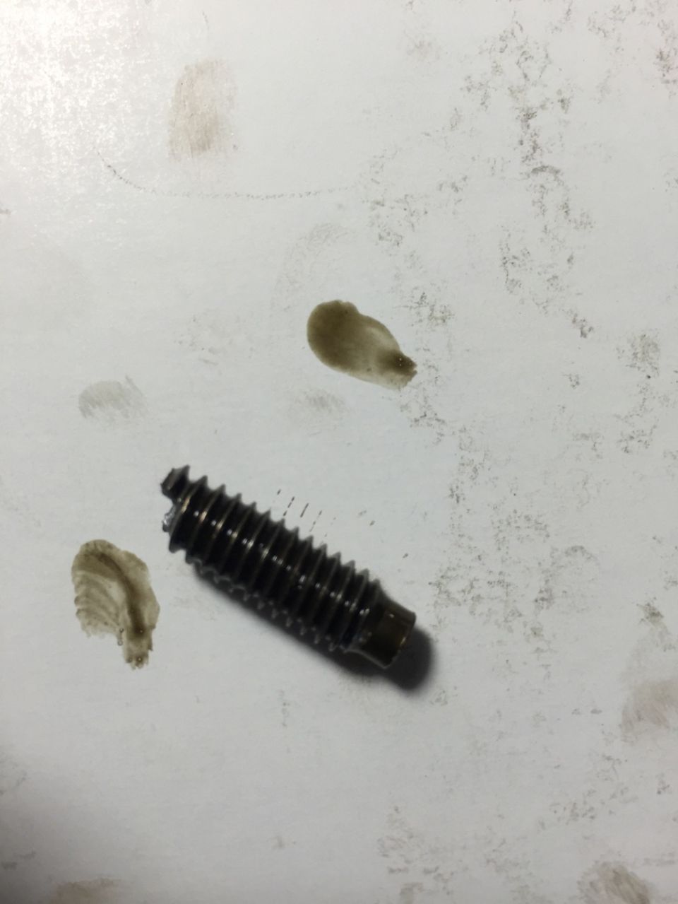 Threaded bolt with oil stains on a white surface